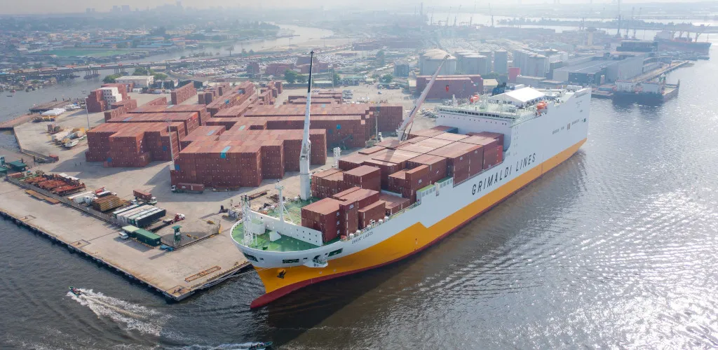 Grimaldi Lines cargo ship docked at a busy container port with cargo stacked along the quay.