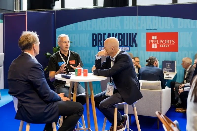 Three Breakbulk Europe attendees networking at a table in the Global Shipper lounge.