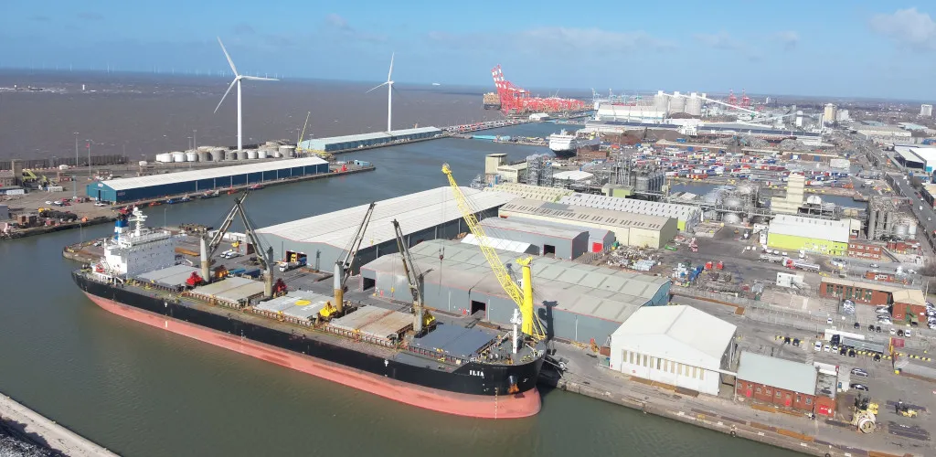 Cargo ship docked at the Port of Liverpool, with cranes, wind turbines and port facilities.