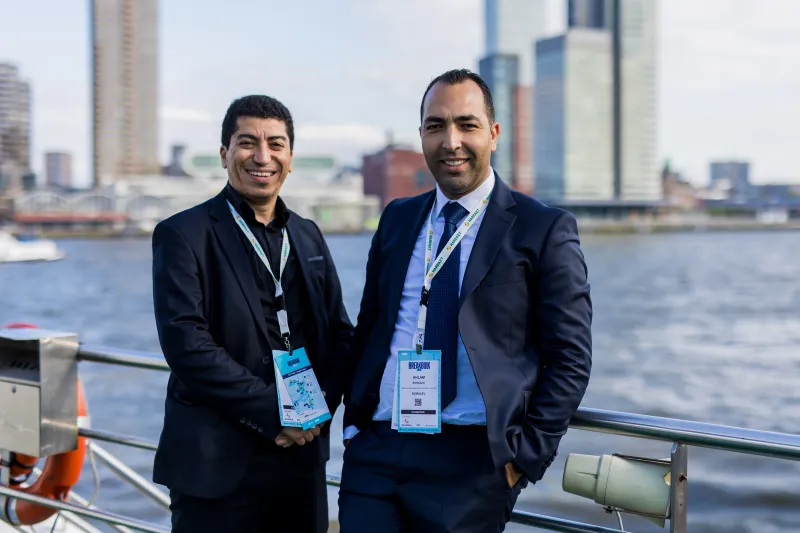 Two Breakbulk Europe attendees by the waterfront, with a city skyline in the background.